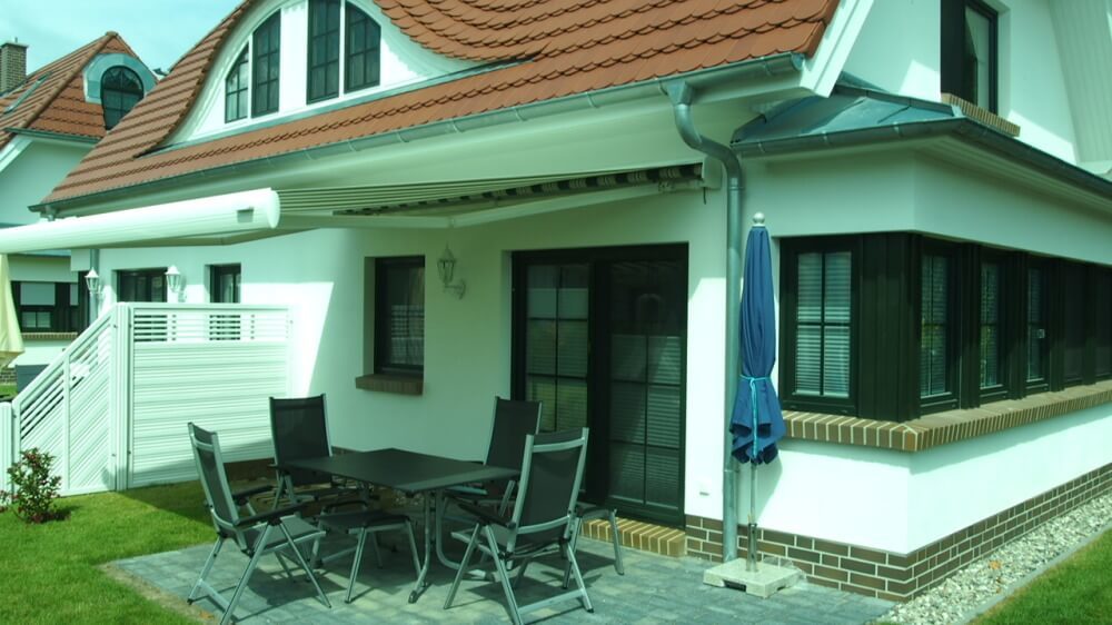 Terrasse mit Gartentisch und Gartenstühlen, elektrischer Markise und Sonnenschirm.